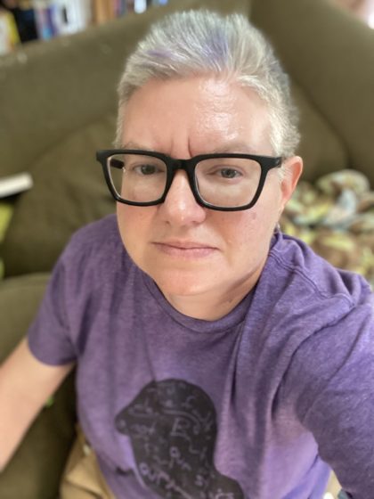 image of a white haired woman in dark glasses and a purple t-shirt